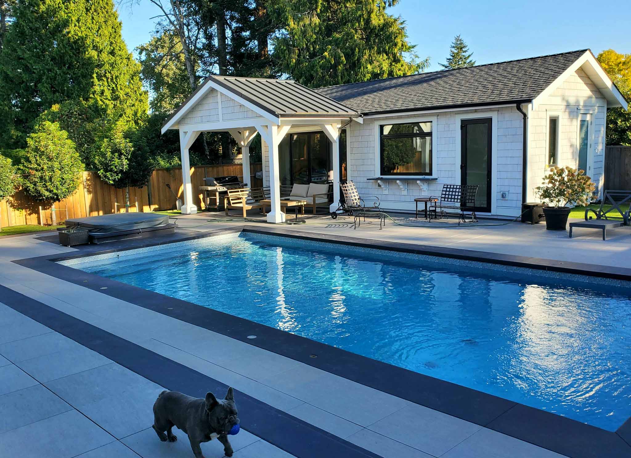 A white and black pool house with a little dog running around, choose our Sacramento pool house builder.